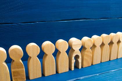 Foto: Holzfiguren in einer Reihe, eine hat ein ausgeschnittenes Kind